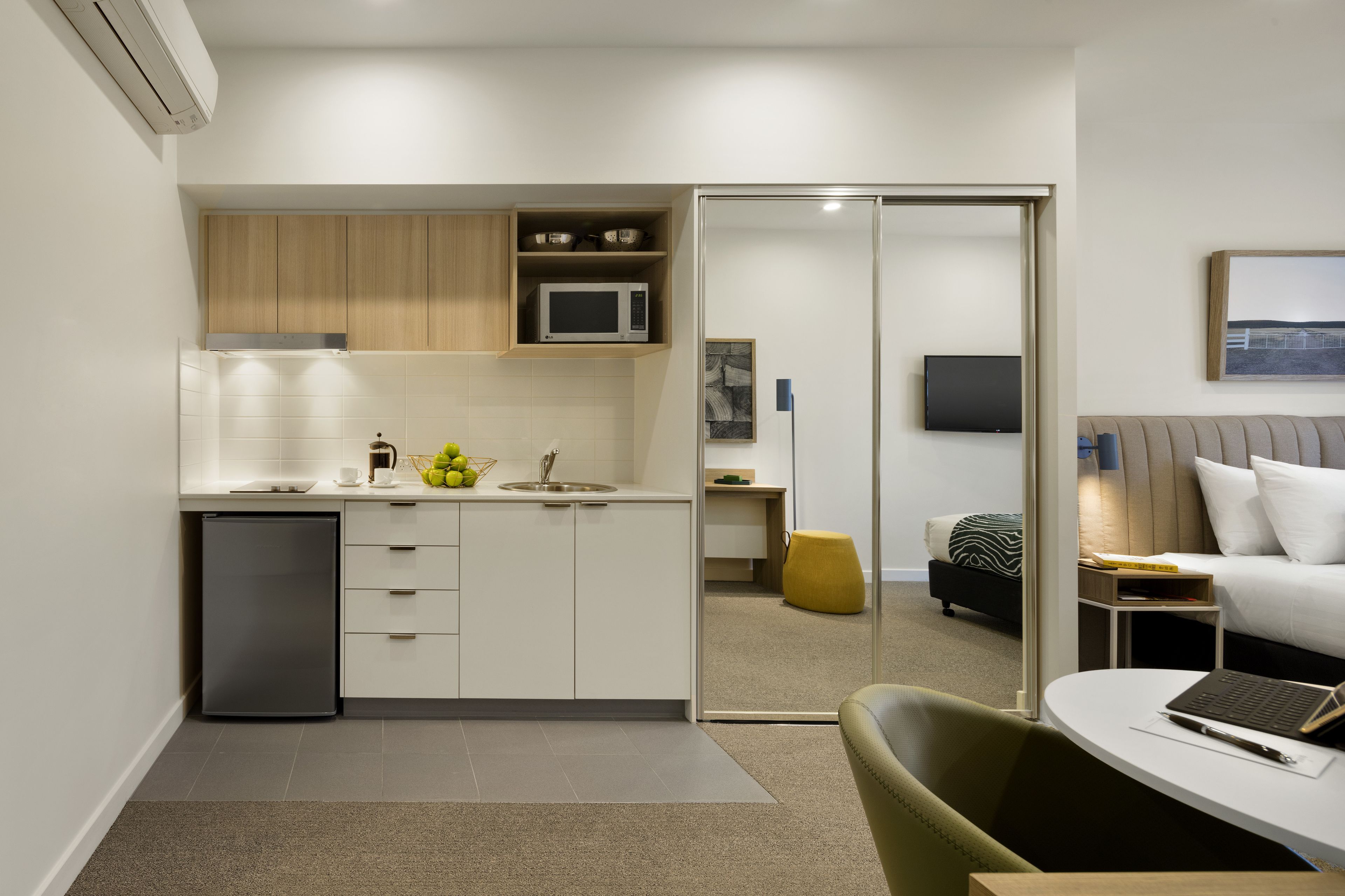 A compact hotel room with a kitchenette, a bed, a desk, and a chair.