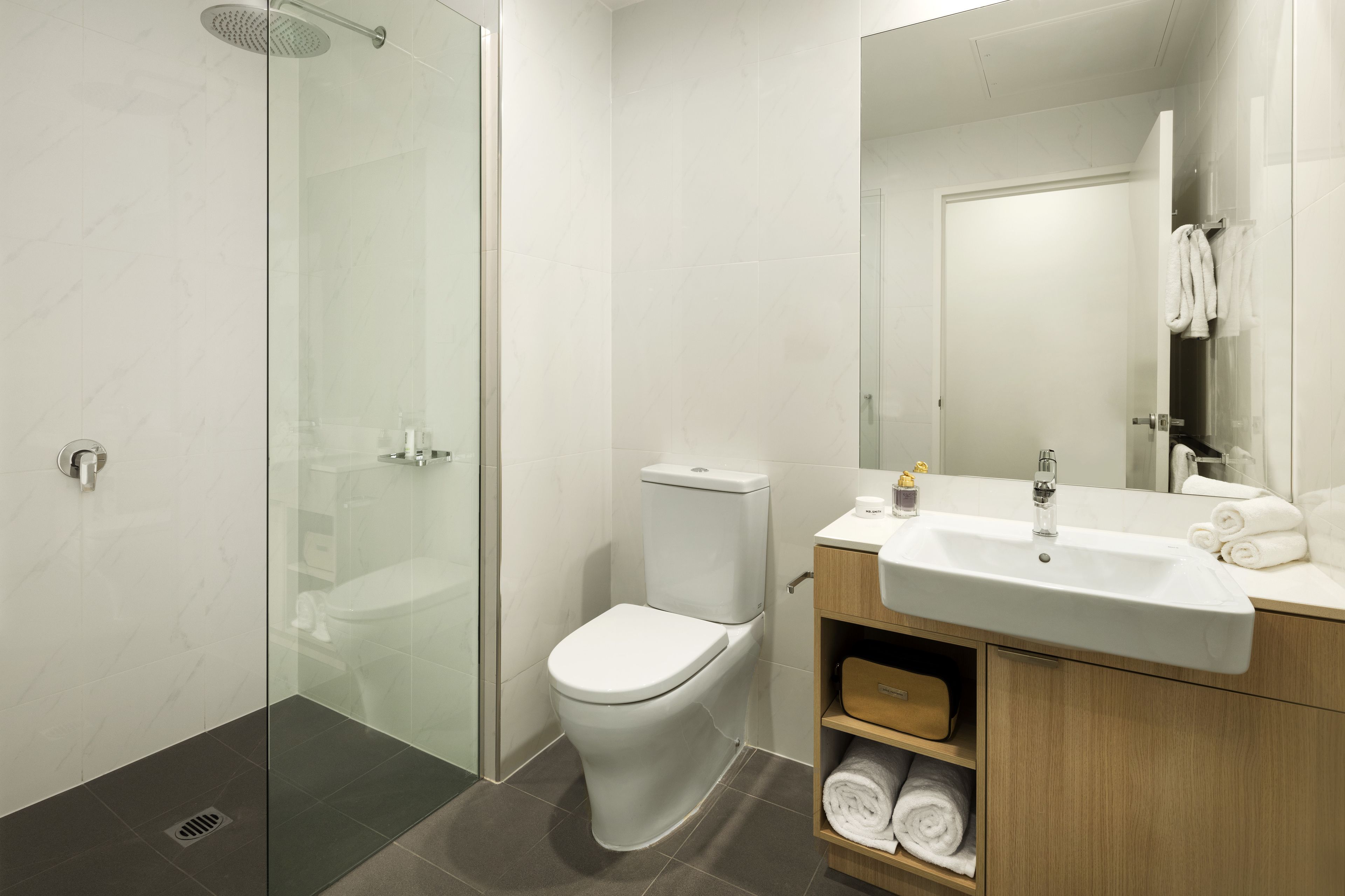 A modern bathroom with a glass-enclosed shower, a white toilet, and a wooden vanity with a sink and towel storage.
