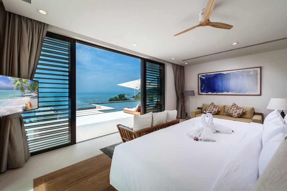 Ein modernes Hotelzimmer mit einem großen Bett, einem Deckenventilator, einem Fernseher und Meerblick.