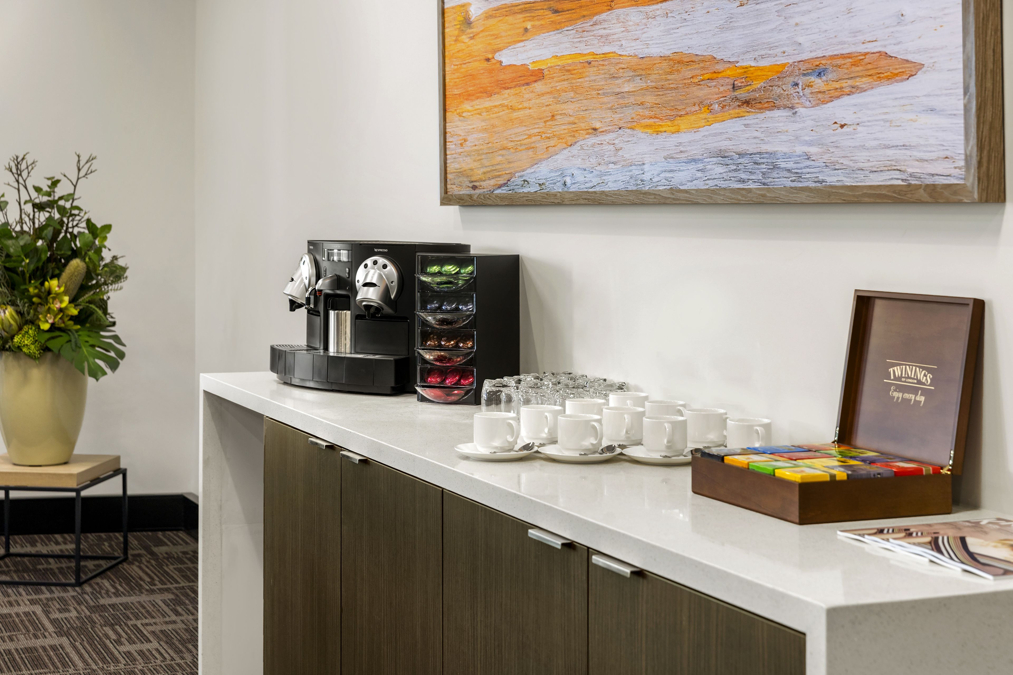 A reception area with a coffee machine, a potted plant, and a framed sign on the counter.