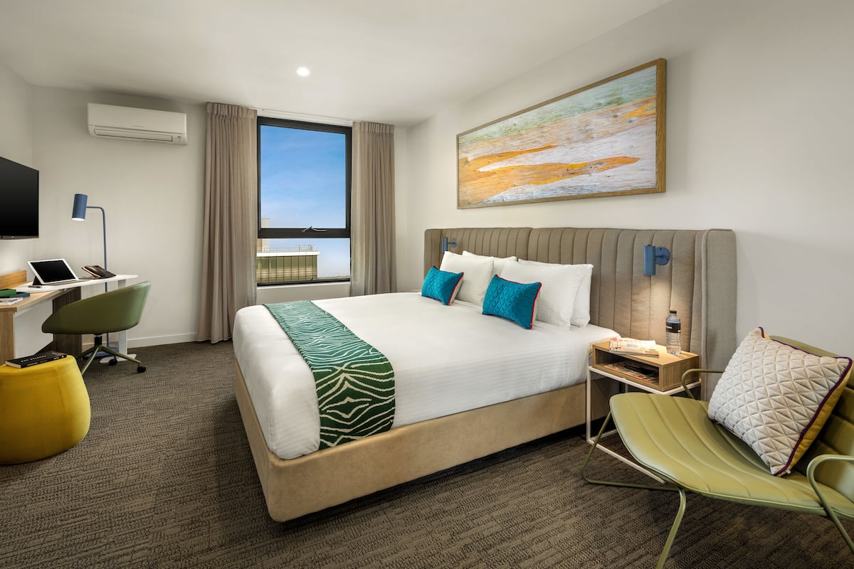 Habitación de hotel con una cama grande, un escritorio con una computadora portátil, una silla, un televisor y una ventana con vistas.