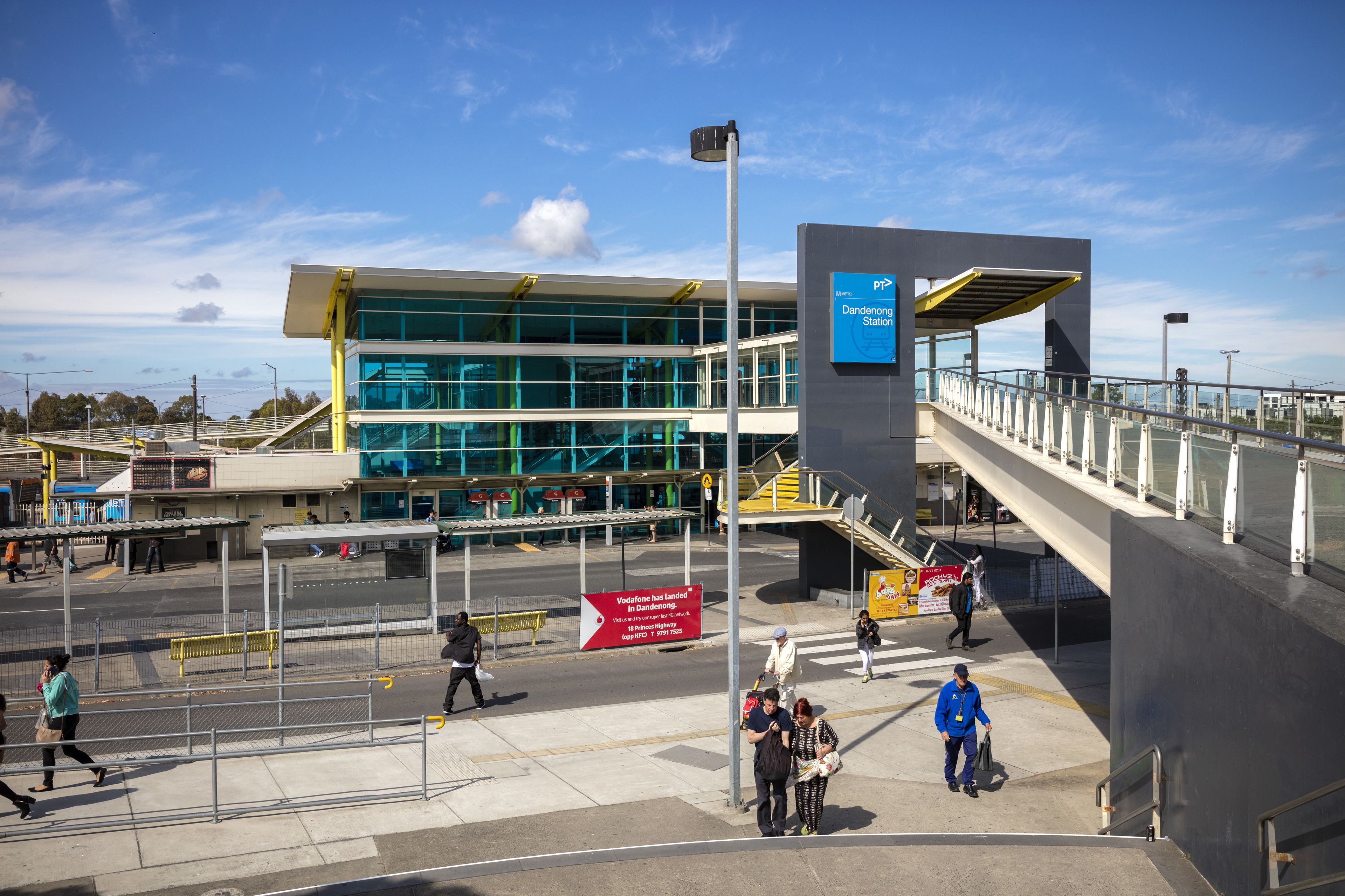Un bâtiment moderne avec une façade en verre, un pont piétonnier et une enseigne indiquant un point de vente Vodafone.
