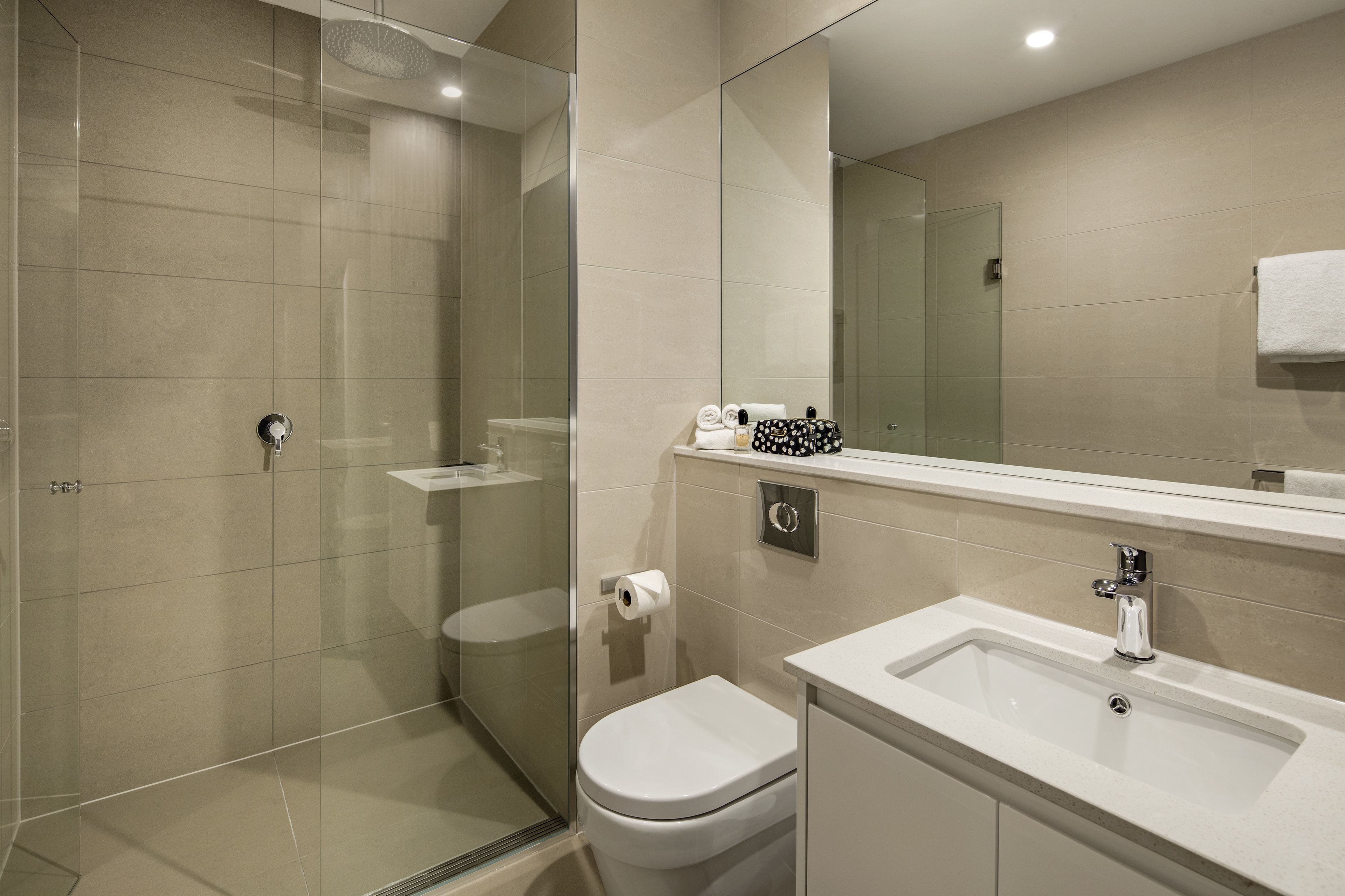 A modern bathroom with a glass shower enclosure, a toilet, and a sink with a mirror above it.