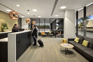A hotel reception area with a modern design, featuring a reception desk labeled "QUEST," a seating area with sofas and chairs, and large windows offering views of the outside. - Quest Dandenong Central (Dandenong)