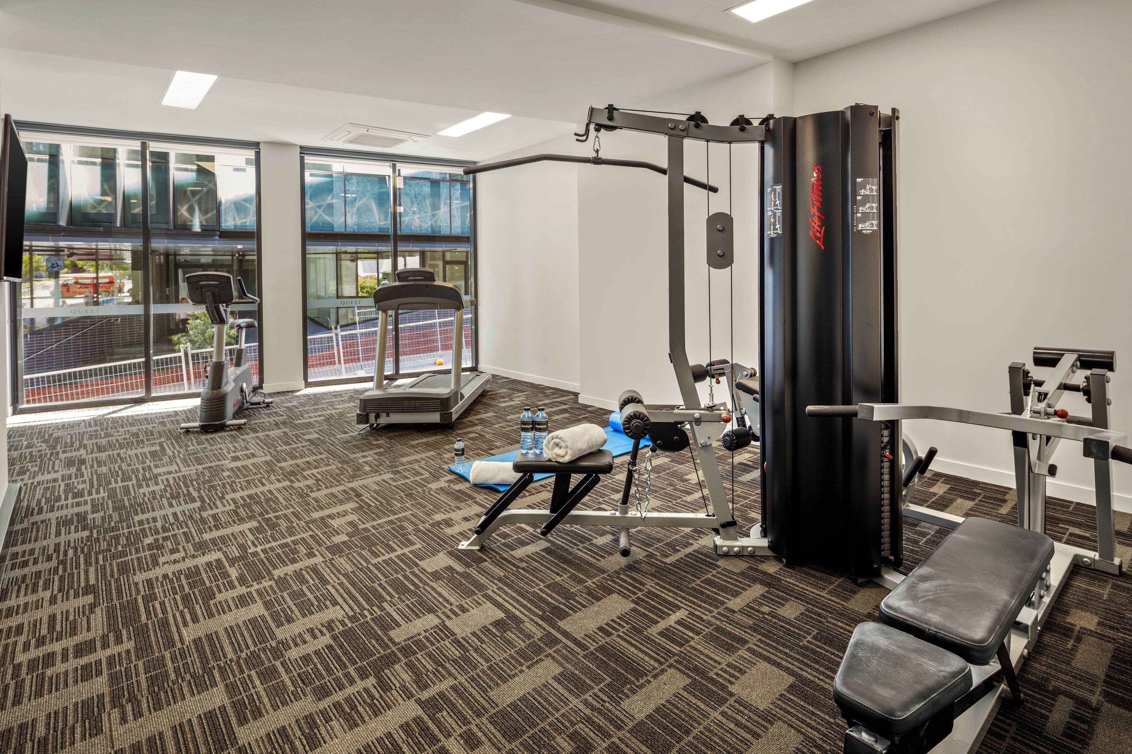 Ein Fitnessraum mit Trainingsgeräten, einer Bank und einer Wasserflasche auf einer Matte.