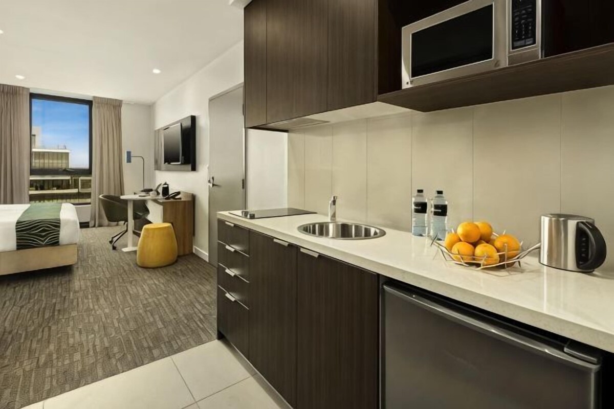 Una habitación de hotel moderna con kitchenette, cama, escritorio y vistas a la ciudad.