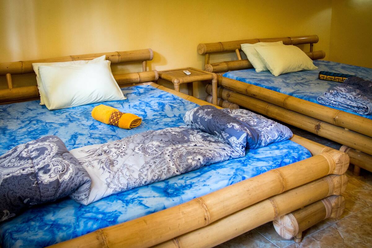 Dos camas con estructura de bambú, ropa de cama estampada en azul, almohadas y una toalla enrollada.