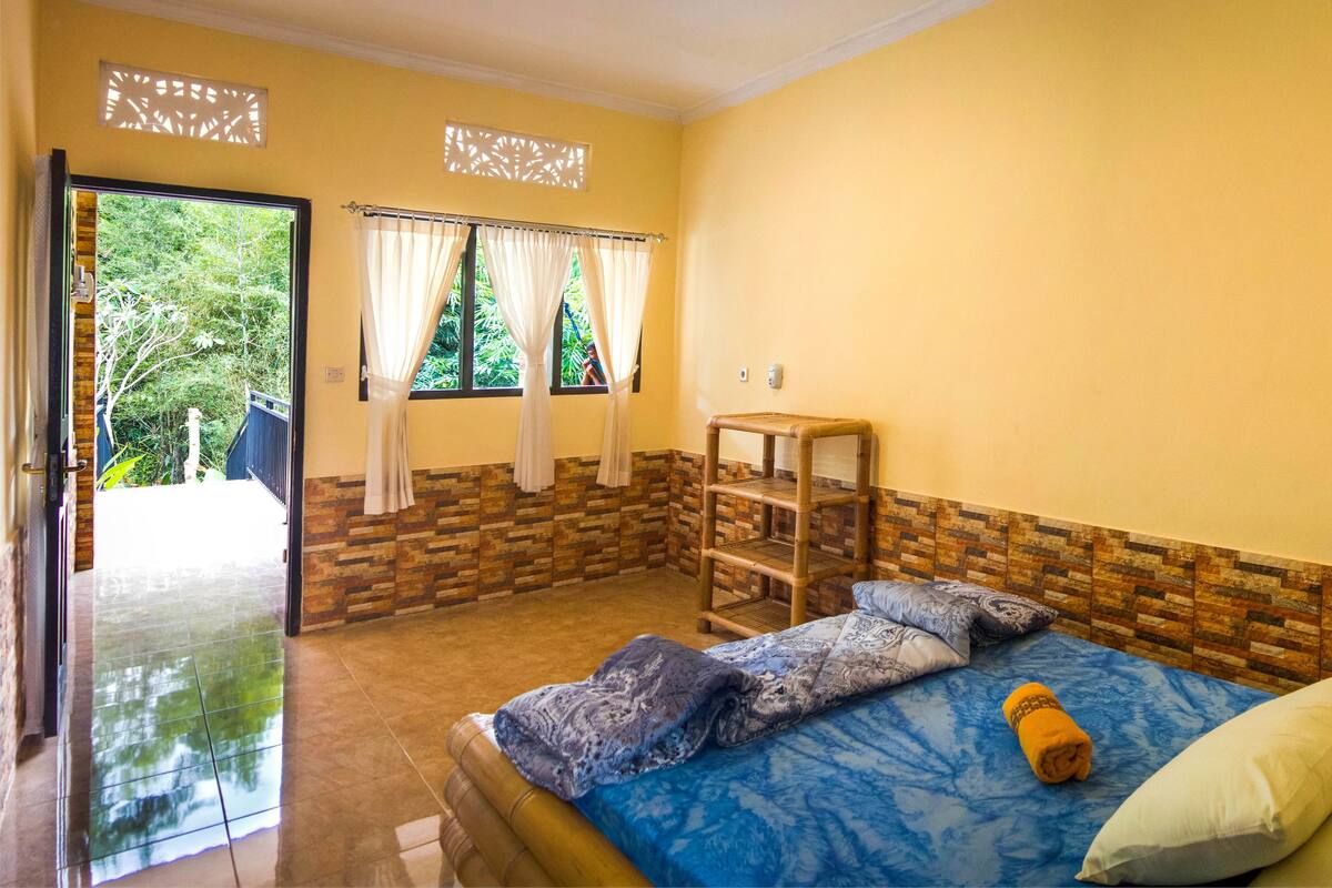 Una habitación con una cama, un taburete de madera pequeño y una ventana con cortinas.
