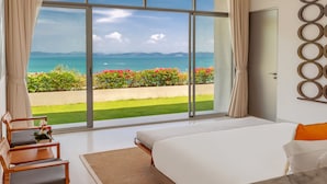 Un dormitorio con un ventanal grande, una cama, una silla y vistas al mar y a las montañas.