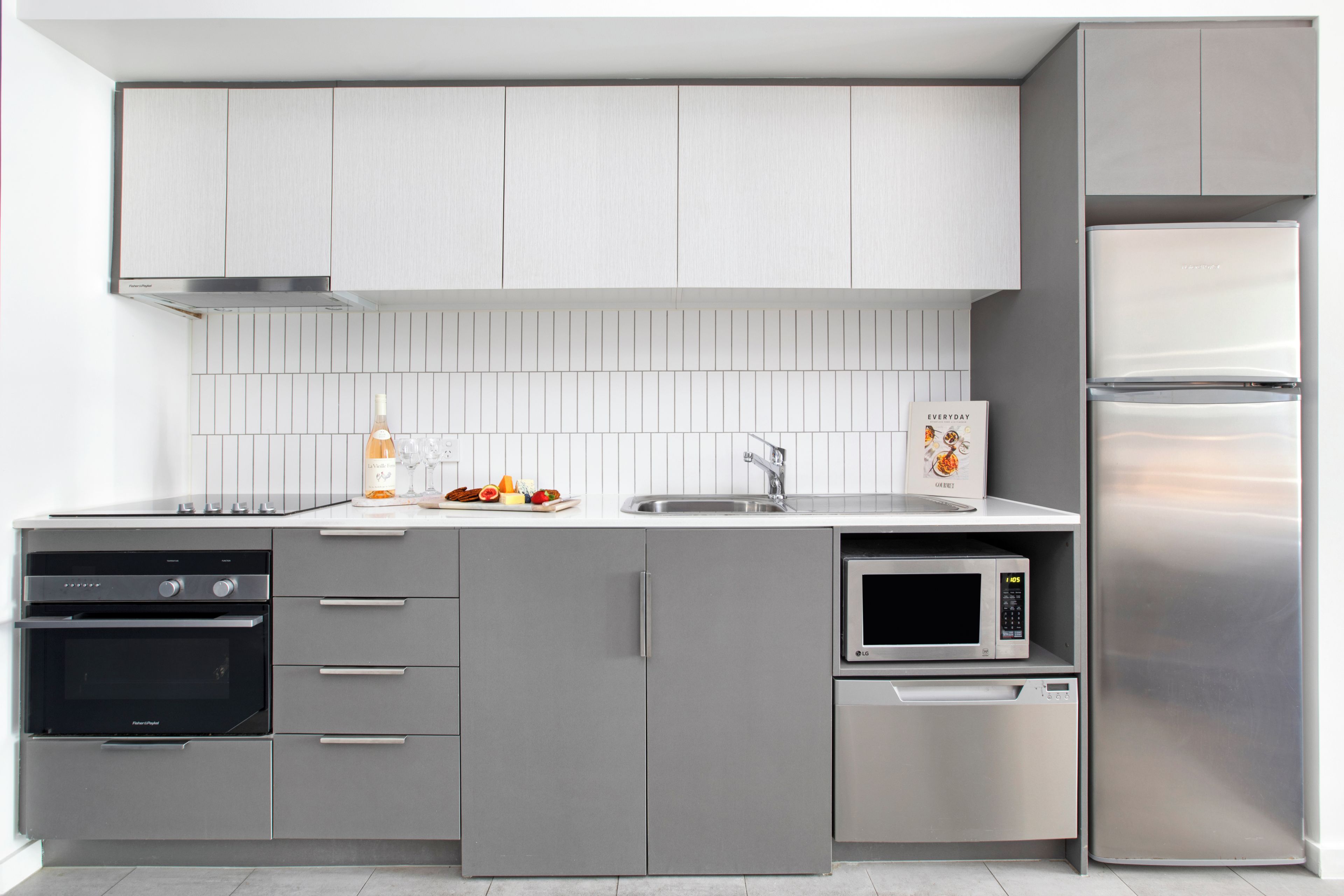 Een moderne keuken met grijze kastjes, een roestvrijstalen koelkast, een inbouwoven, een magnetron en een vaatwasser.