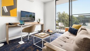 Una sala de estar moderna con un sofá, una mesa de centro, un escritorio con una computadora y un amplio ventanal que ofrece vistas al exterior.
