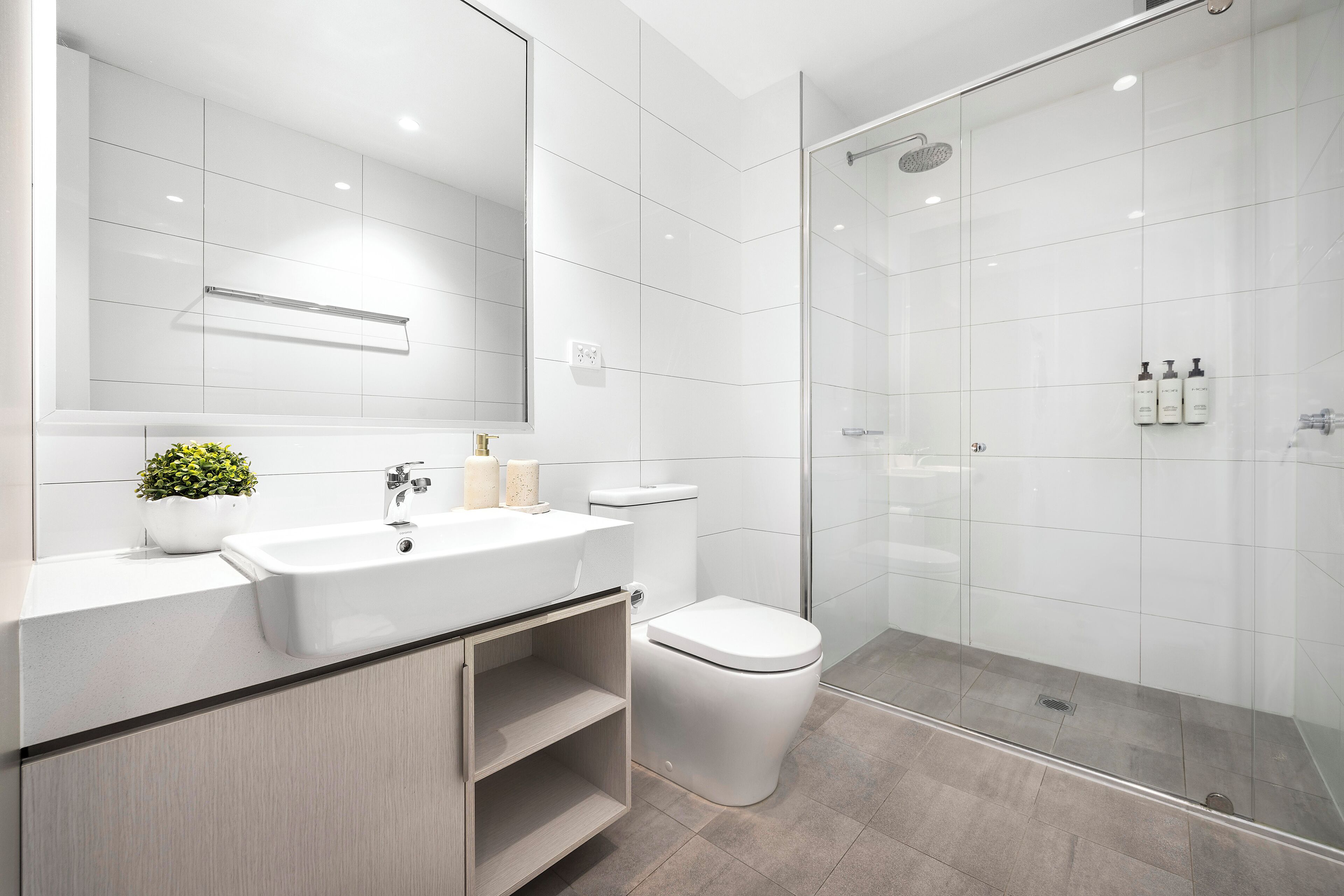A modern bathroom with a white sink, toilet, and glass shower enclosure.