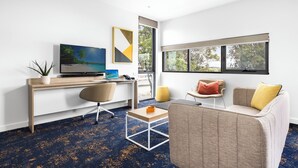 Una sala de estar moderna con un televisor grande, un escritorio, un sofá cómodo y un ventanal con vistas a árboles.