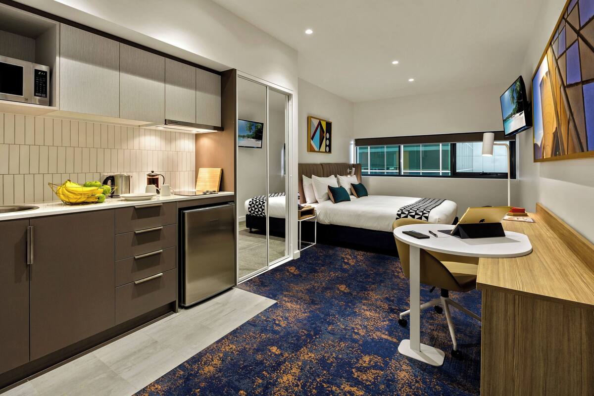 Una habitación de hotel moderna con cocina, cama con vistas y escritorio con computadora portátil.