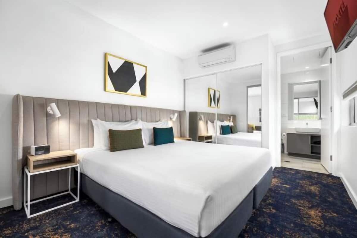 Habitación de hotel con una cama grande, mesitas de noche, un espejo y un baño visible a través de una puerta abierta.
