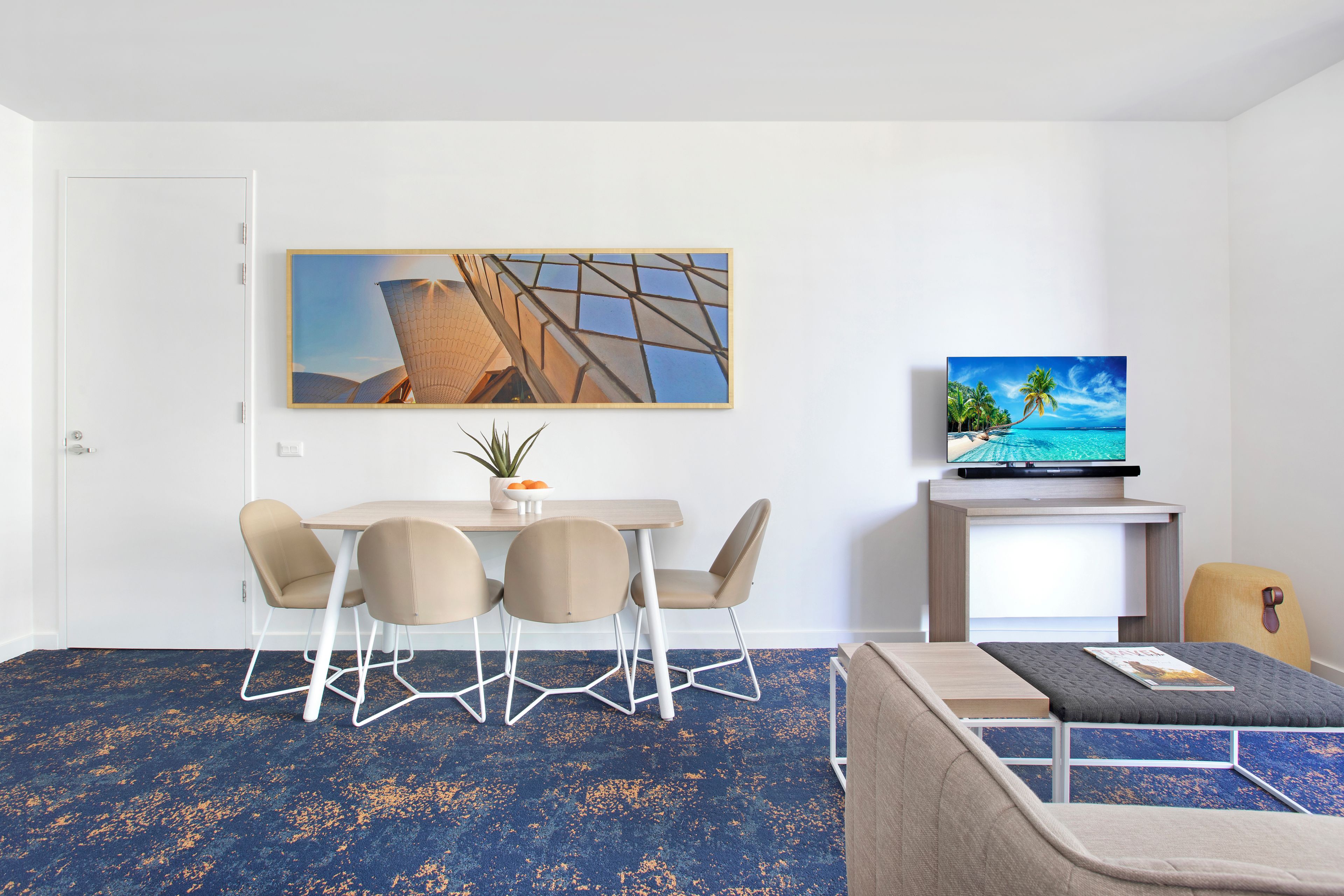 Une chambre d’hôtel moderne dotée d’un coin repas, d’un téléviseur à écran plat et d’un grand tableau.