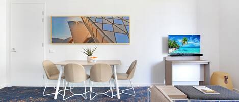 Une chambre d’hôtel moderne dotée d’un coin repas, d’un téléviseur à écran plat et d’un grand tableau.