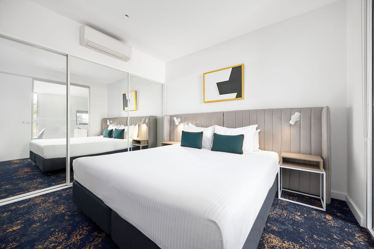 Una habitación de hotel con una cama grande, una mesita de noche, un espejo y un cuadro colgado en la pared.
