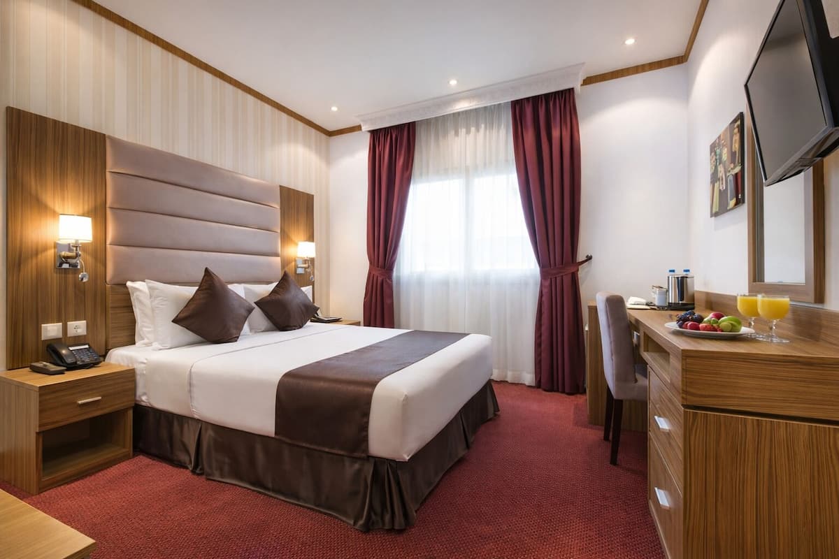 A hotel room with a large bed, bedside tables, a desk with a chair, a television, and a window with curtains.