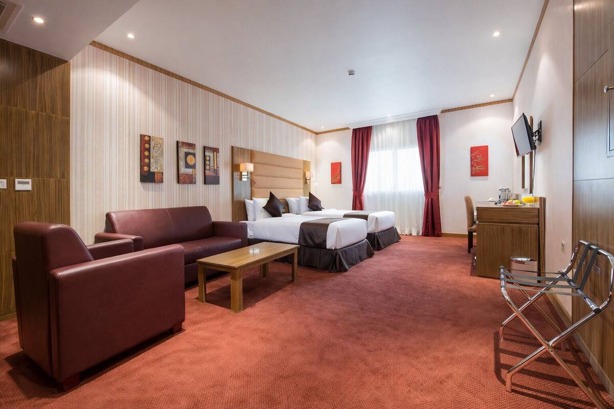 A hotel room with a sofa, two beds, a desk, and a TV.