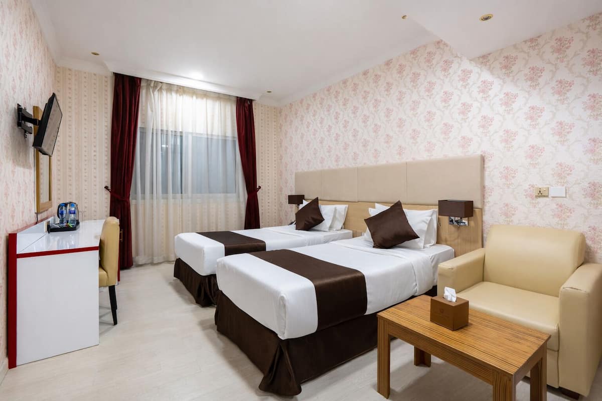 A hotel room with two beds, a desk, a chair, and a small table.
