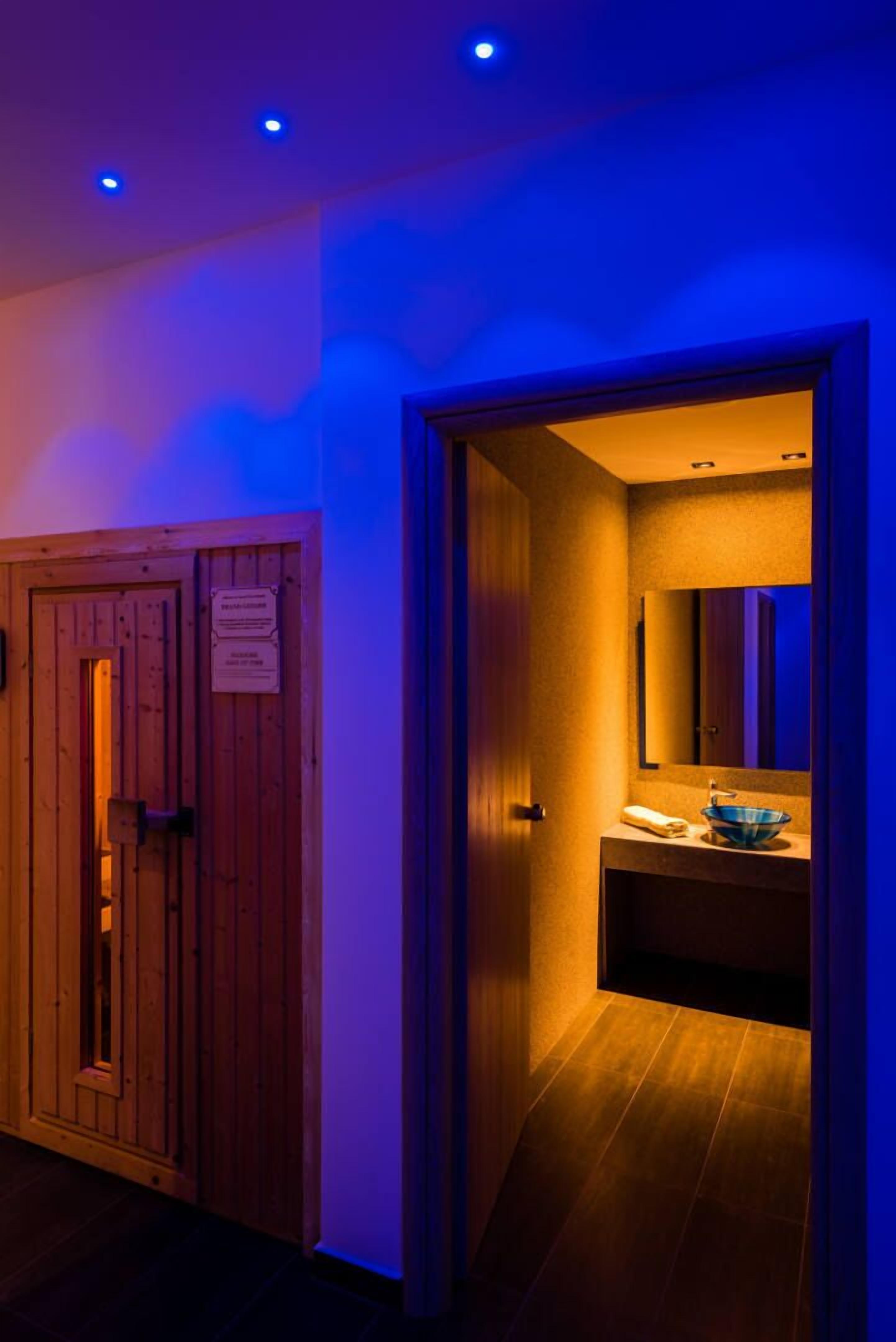 Una puerta de madera con un letrero, un baño con un lavabo azul y un espejo, y un pasillo iluminado en azul.