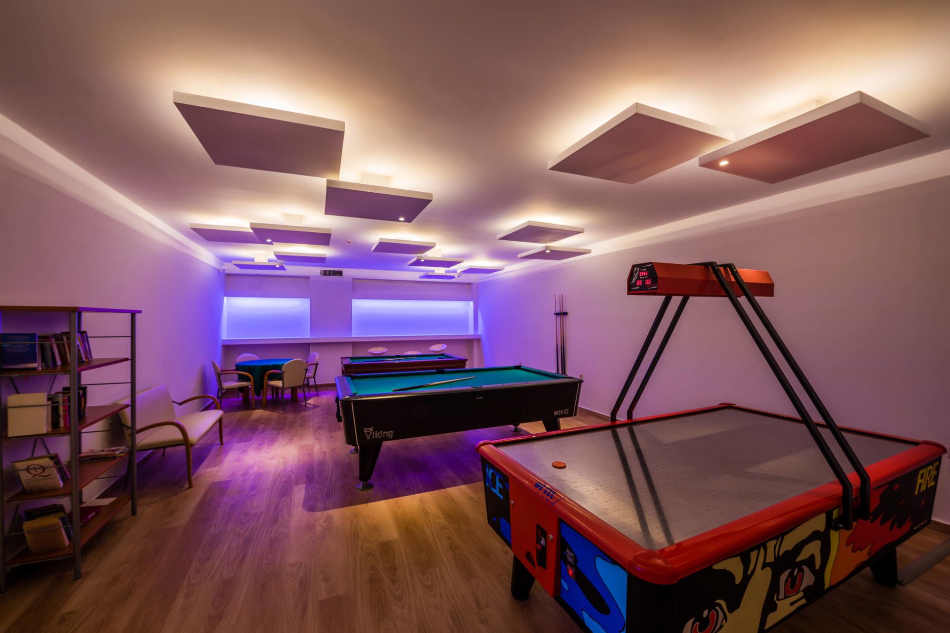A pool room with two pool tables, a billiard cue rack, and a bookshelf.