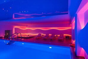 Um spa moderno com piscina, espreguiçadeiras e um design de iluminação em forma de onda nas paredes.