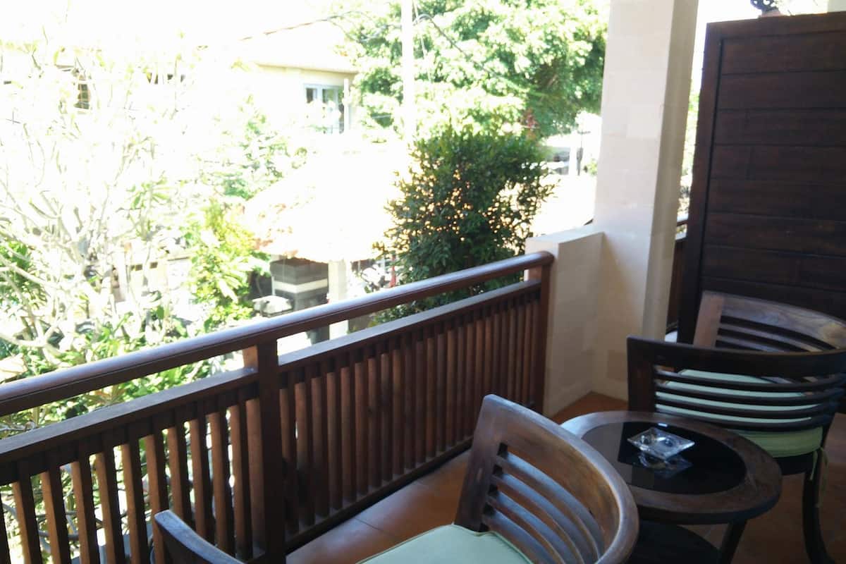 A balcony with a wooden railing, a cushioned chair, and a small round table with a glass object on it.