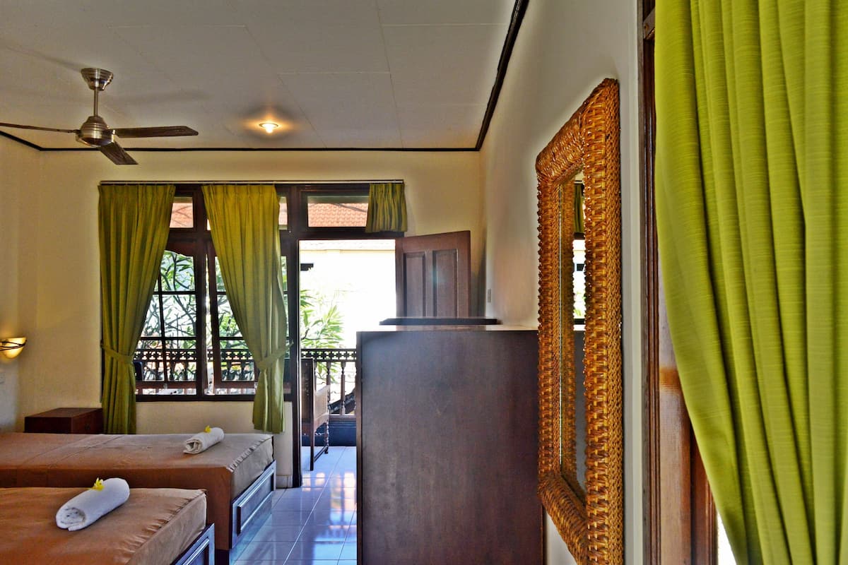 A hotel room with two beds, a ceiling fan, a large mirror, and green curtains.