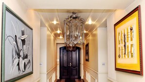 Un pasillo con candelabro, obras de arte enmarcadas y una puerta de madera oscura.