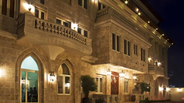 Un edificio de piedra con ventanas arqueadas y un balcón, iluminado por luces exteriores.