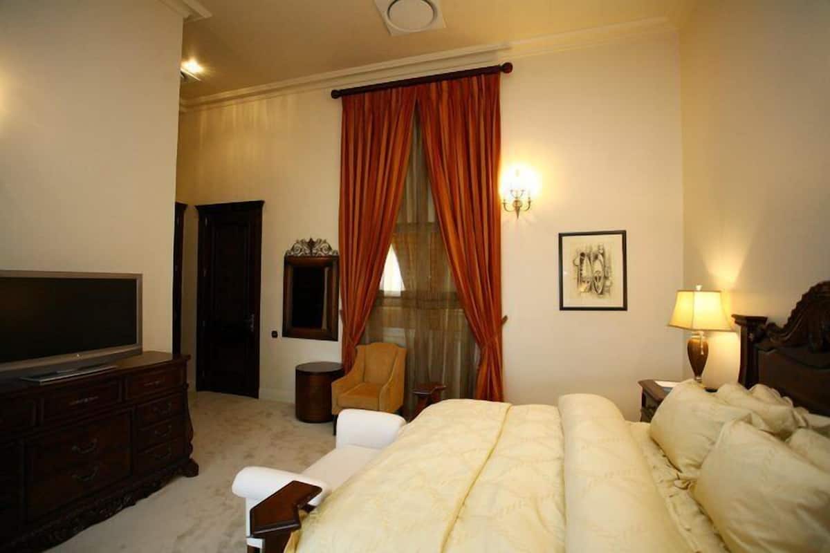 A hotel room with a large bed, a television, a chair, a desk, and a window with curtains.
