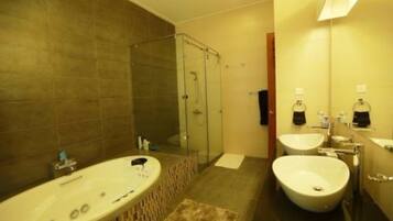 A modern bathroom with a large bathtub, two sinks, and a glass shower enclosure.
