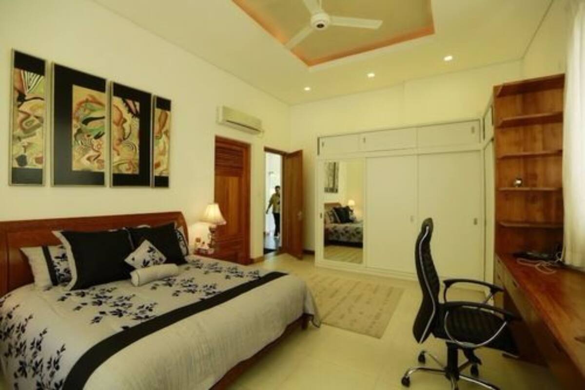 A bedroom with a bed, a desk, and a chair. There is a wardrobe and a door leading to another room.