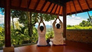 Duas pessoas meditando num quarto com vista para vegetação e montanhas.