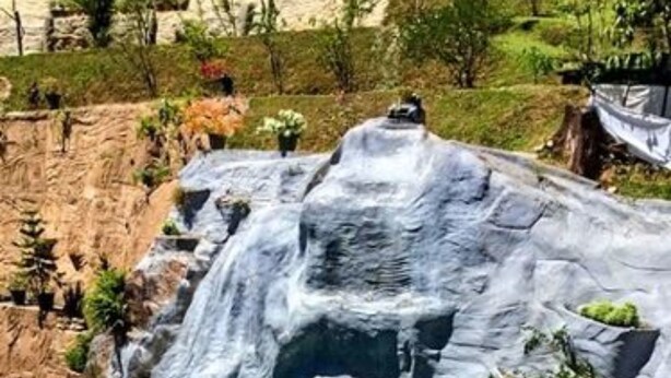 Piscina com cascata, cercada por um muro de pedra e vegetação.