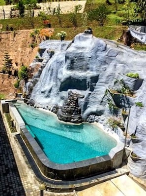 Une piscine agrémentée d’une cascade, entourée d’un mur de pierre et de verdure.
