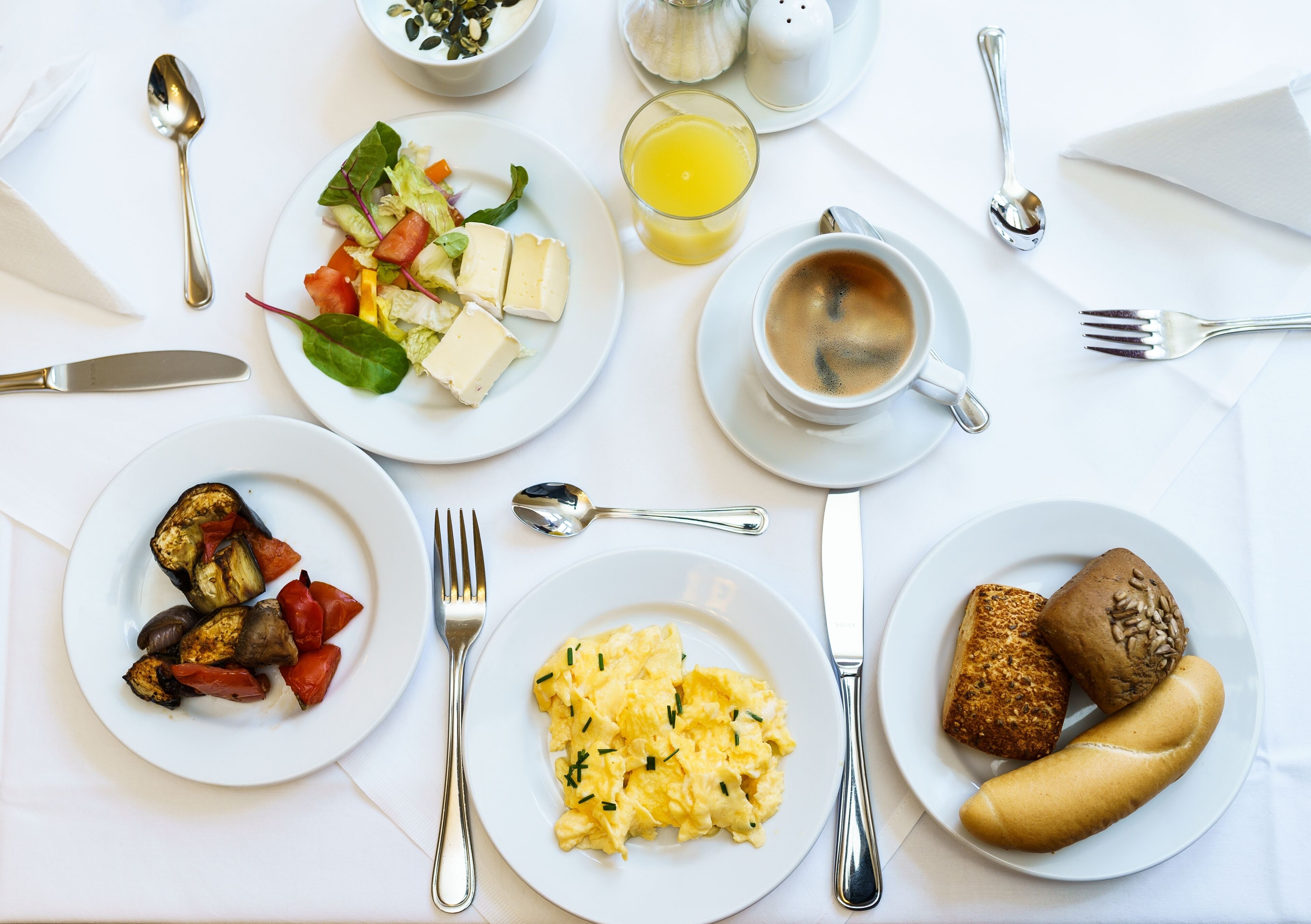 Un desayuno con huevos revueltos, vegetales asados, ensalada de frutas, tostadas y una taza de café.