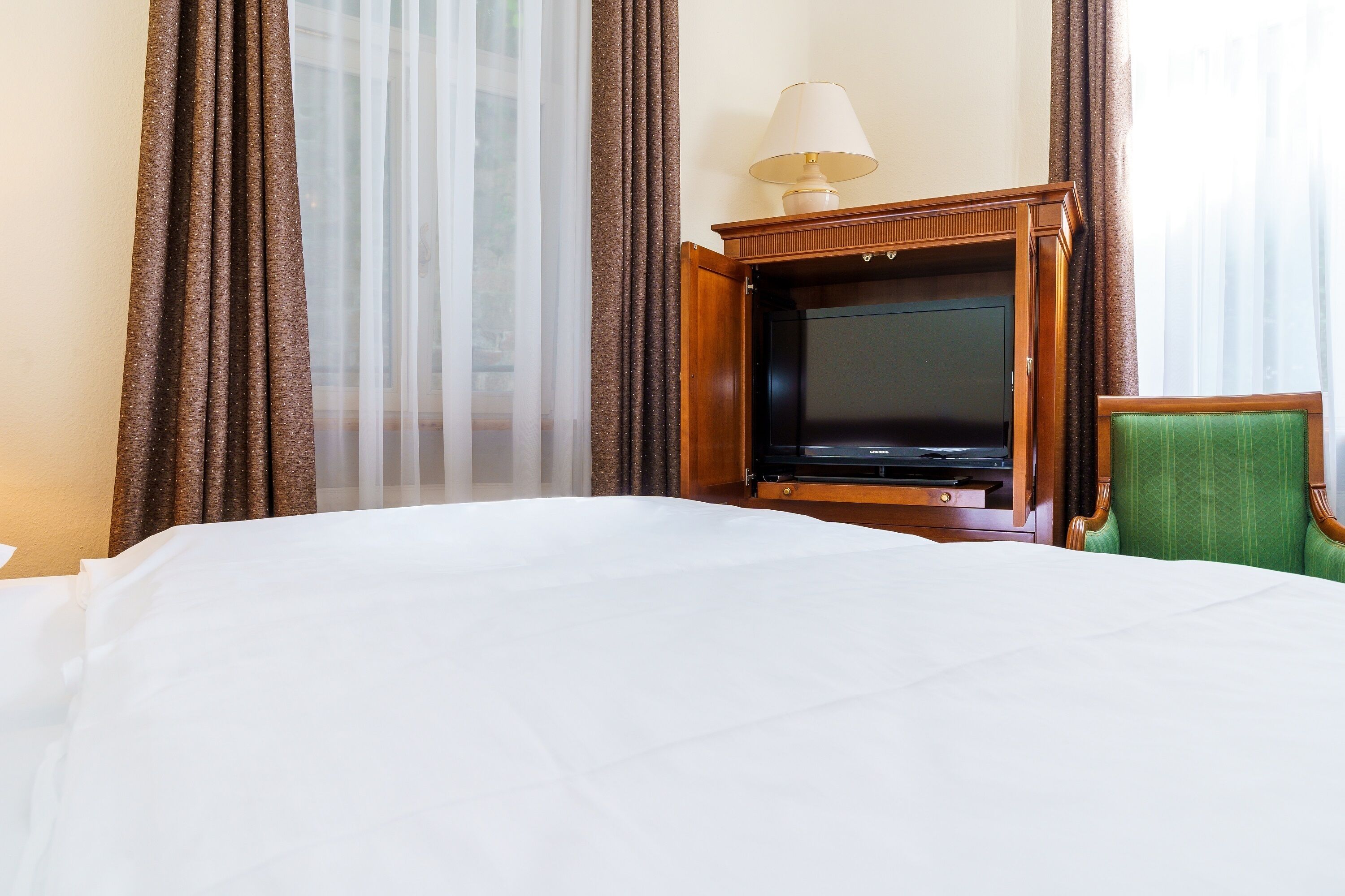 A hotel room with a large bed, a television, a lamp, and a green chair.