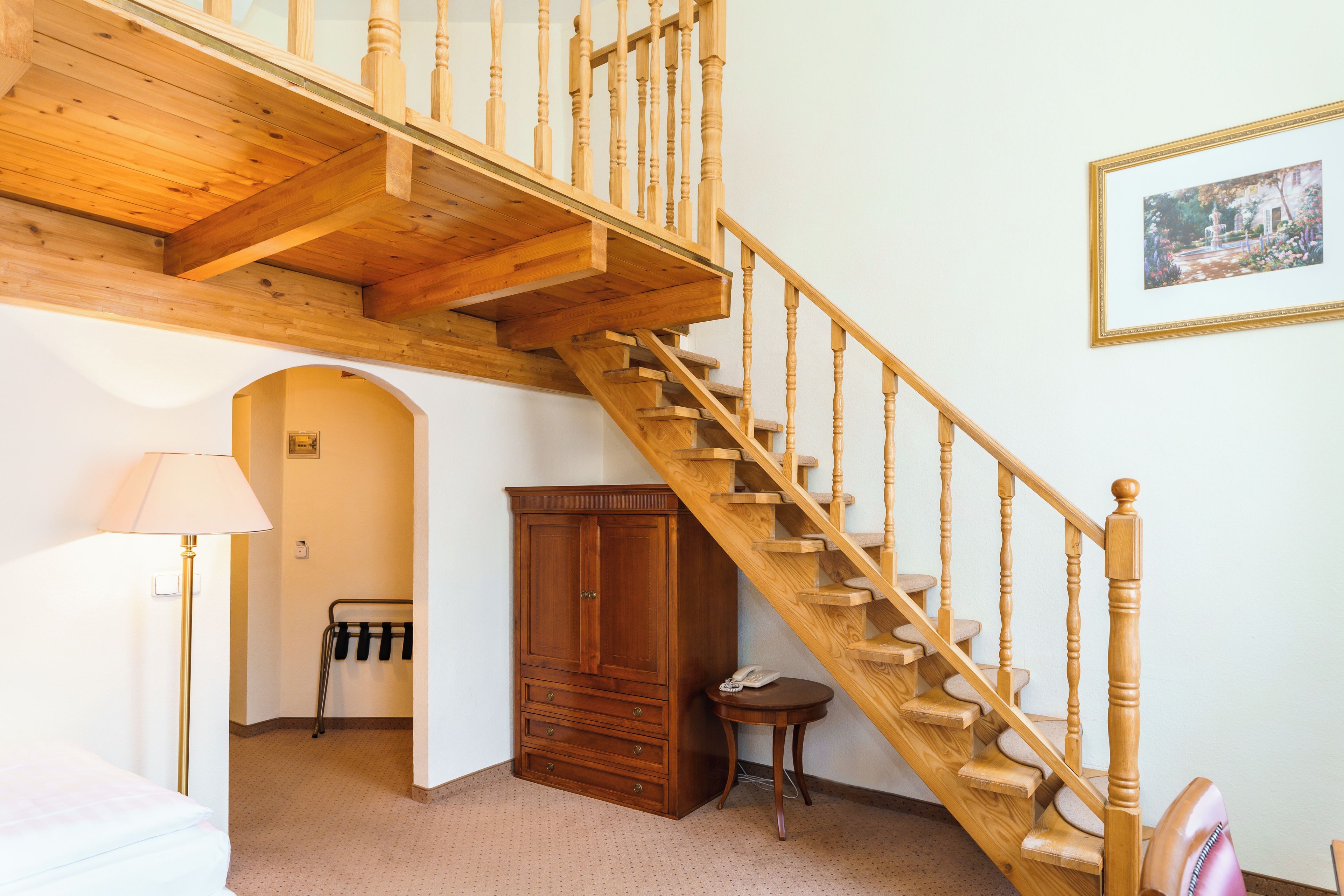 A wooden staircase with a handrail, a wooden cabinet, a lamp, and a framed picture on the wall.
