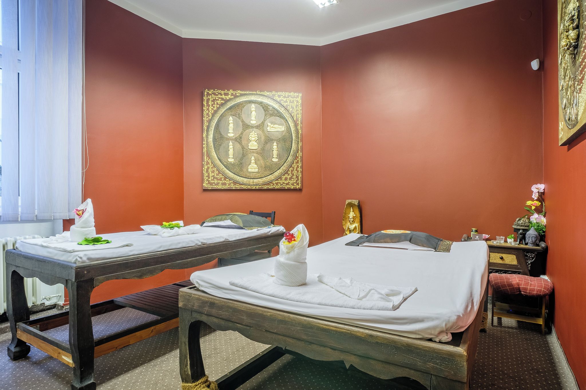 Ein Zimmer mit zwei Betten, einer Massageliege, einem kleinen Schreibtisch und einer Wanddekoration.
