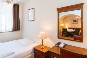 A hotel room with a single bed, a bedside table with a lamp, a mirror, and a framed picture on the wall. - Hotel Anglický Dvůr (Karlovy Vary)