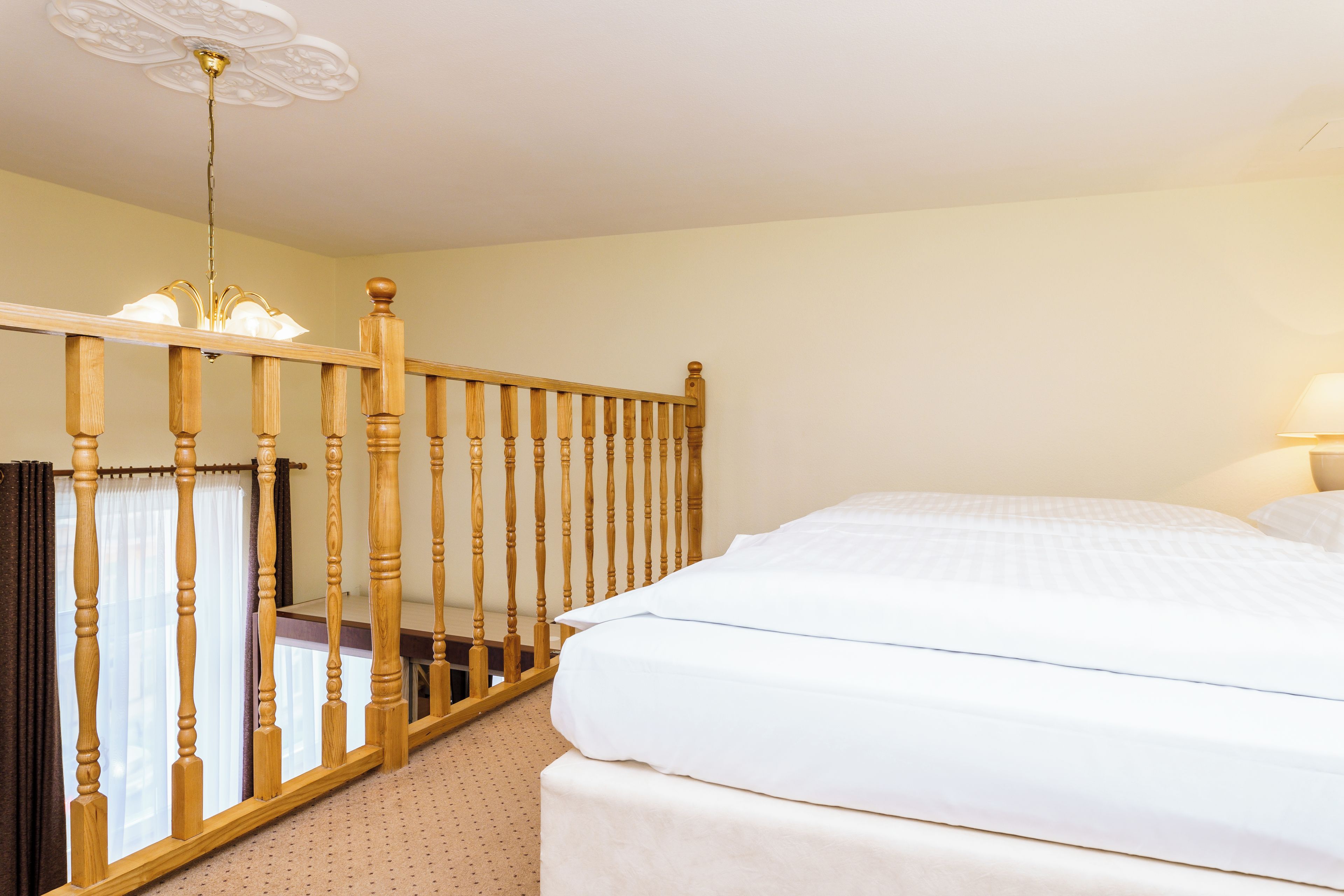 A hotel room with a wooden staircase, a bed with white bedding, and a ceiling light fixture.