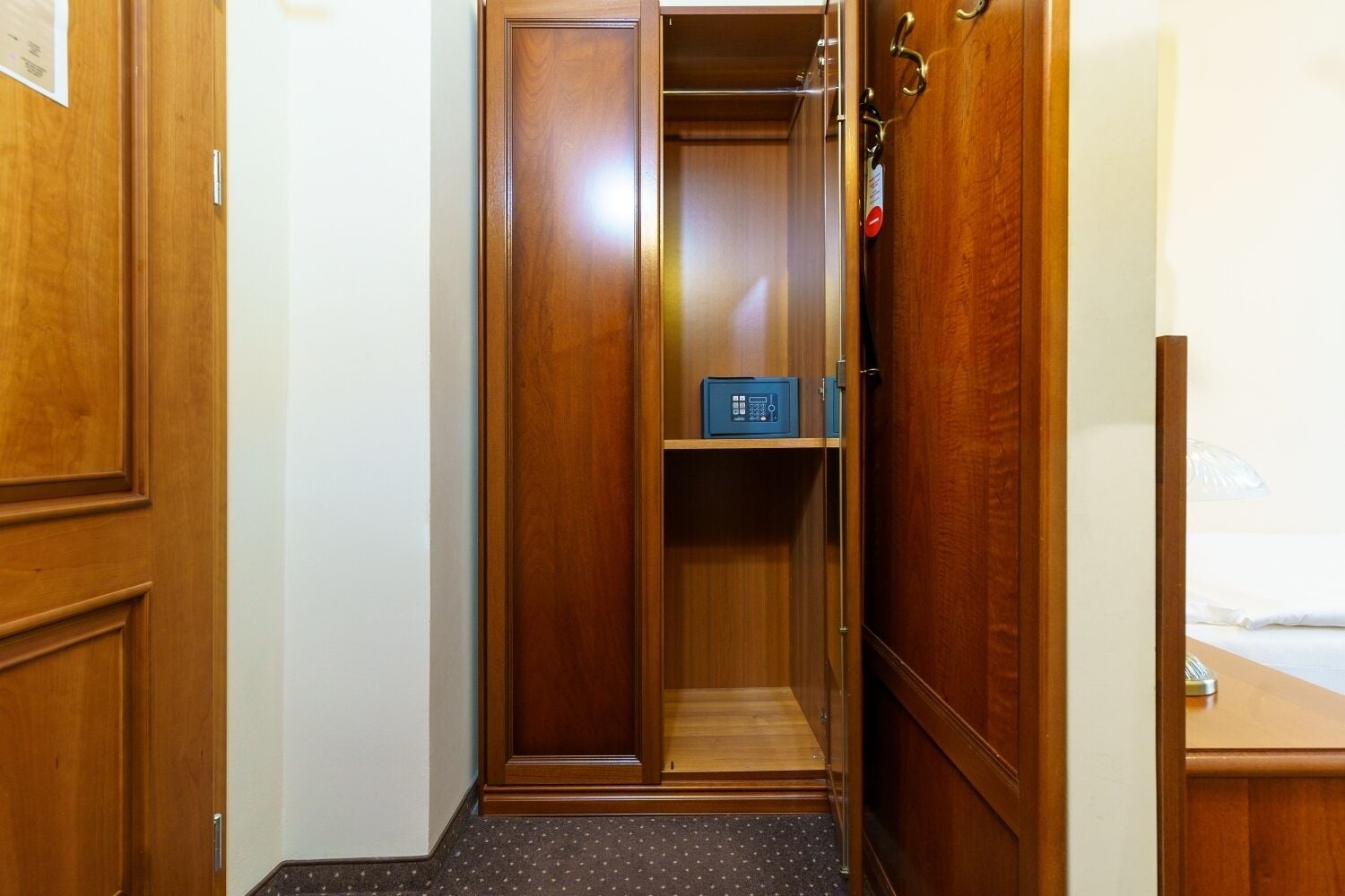 A hotel room with a wooden wardrobe, a small blue safe, and a bed with white bedding.