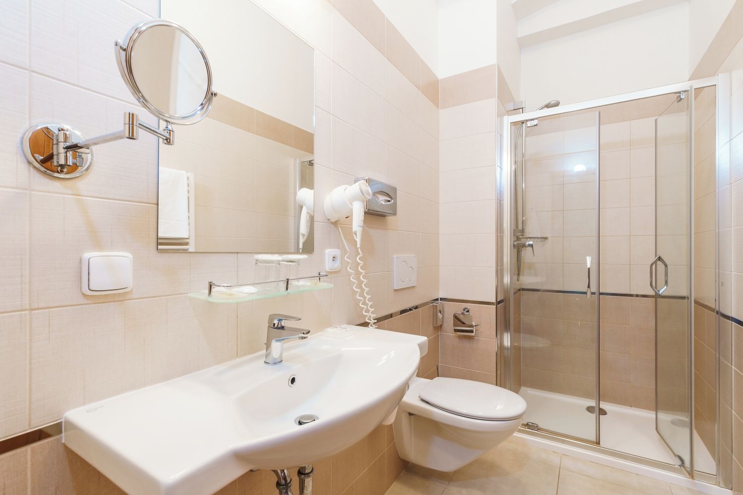 A modern bathroom with a sink, mirror, hairdryer, and a glass-enclosed shower.