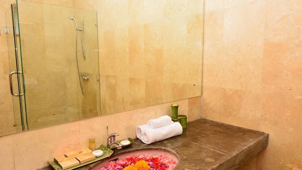Un baño con cabina de ducha de vidrio, un lavabo con artículos de aseo y un arreglo floral decorativo.