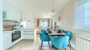 A modern kitchen with white cabinets, a microwave, and a dining area with teal chairs and a table set for two. - Pansion Martin (Podstrana)