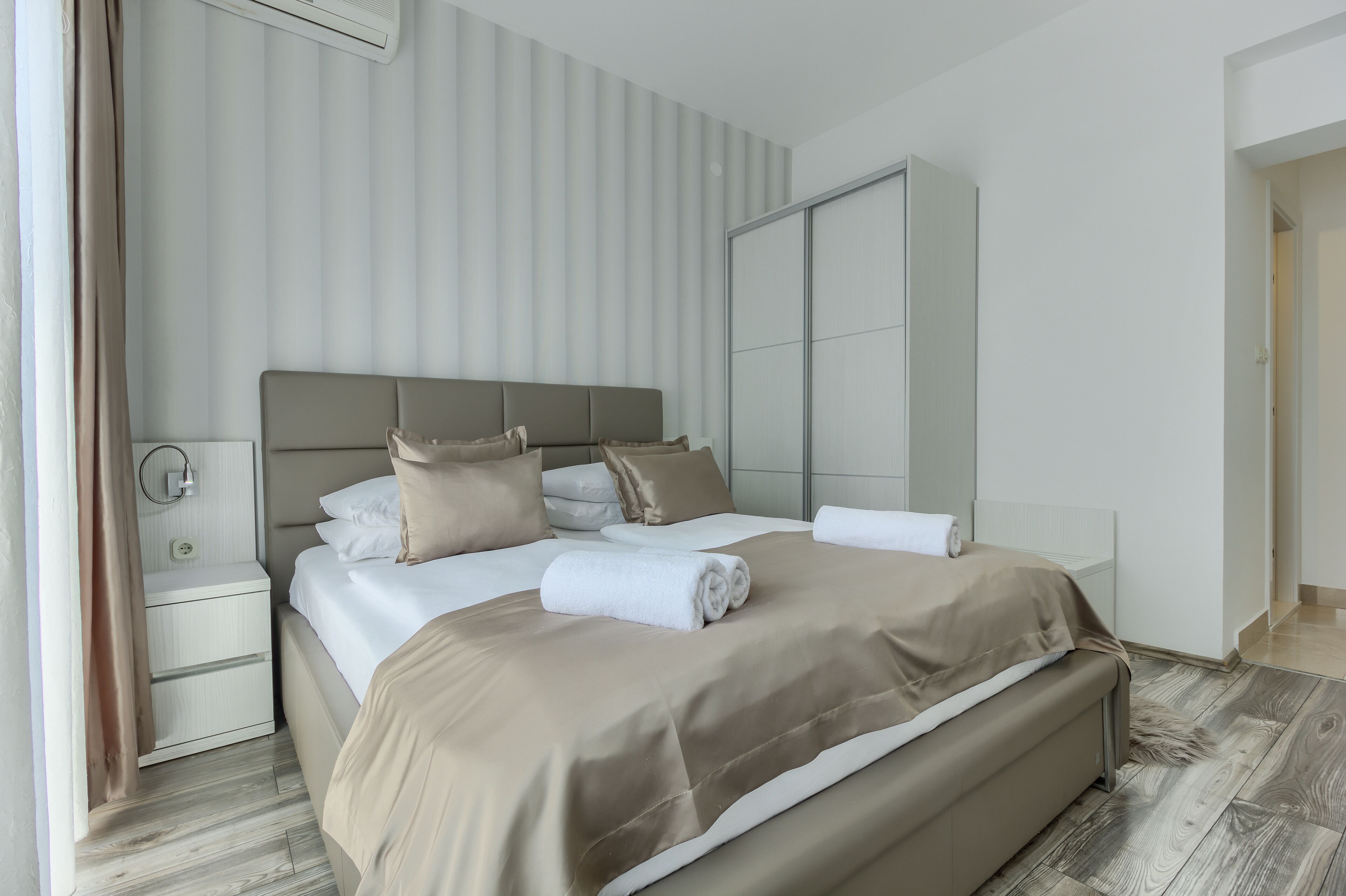 Een moderne slaapkamer met een groot bed, nachtkastje, kledingkast en raam met gordijnen.