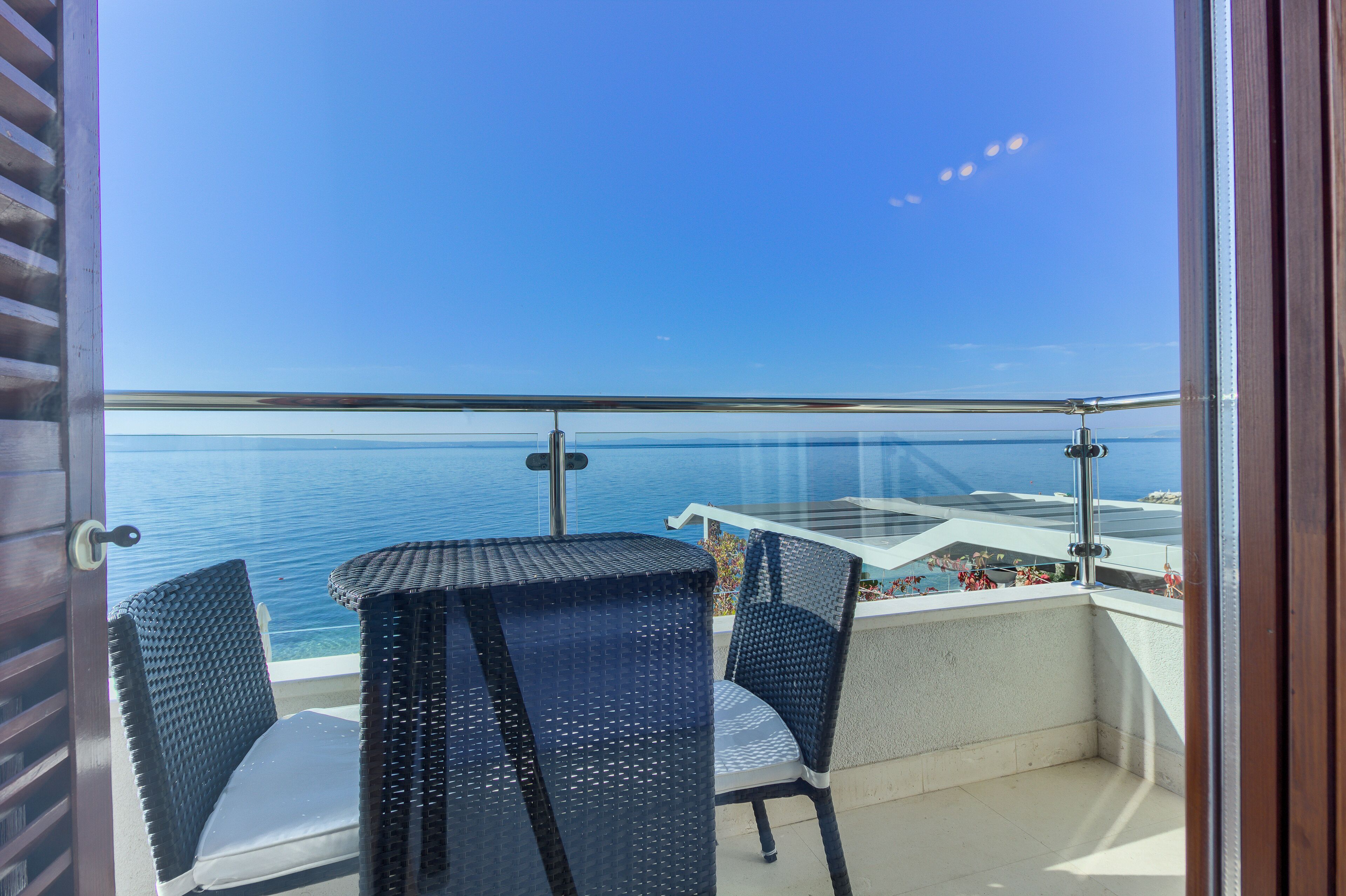 Varanda com vista para o mar, móveis de vime e guarda-corpo de vidro.